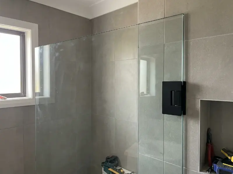 Douchewand in helder gehard glas van acht millimeter met een zwart scharnier, in een betegelde badkamer